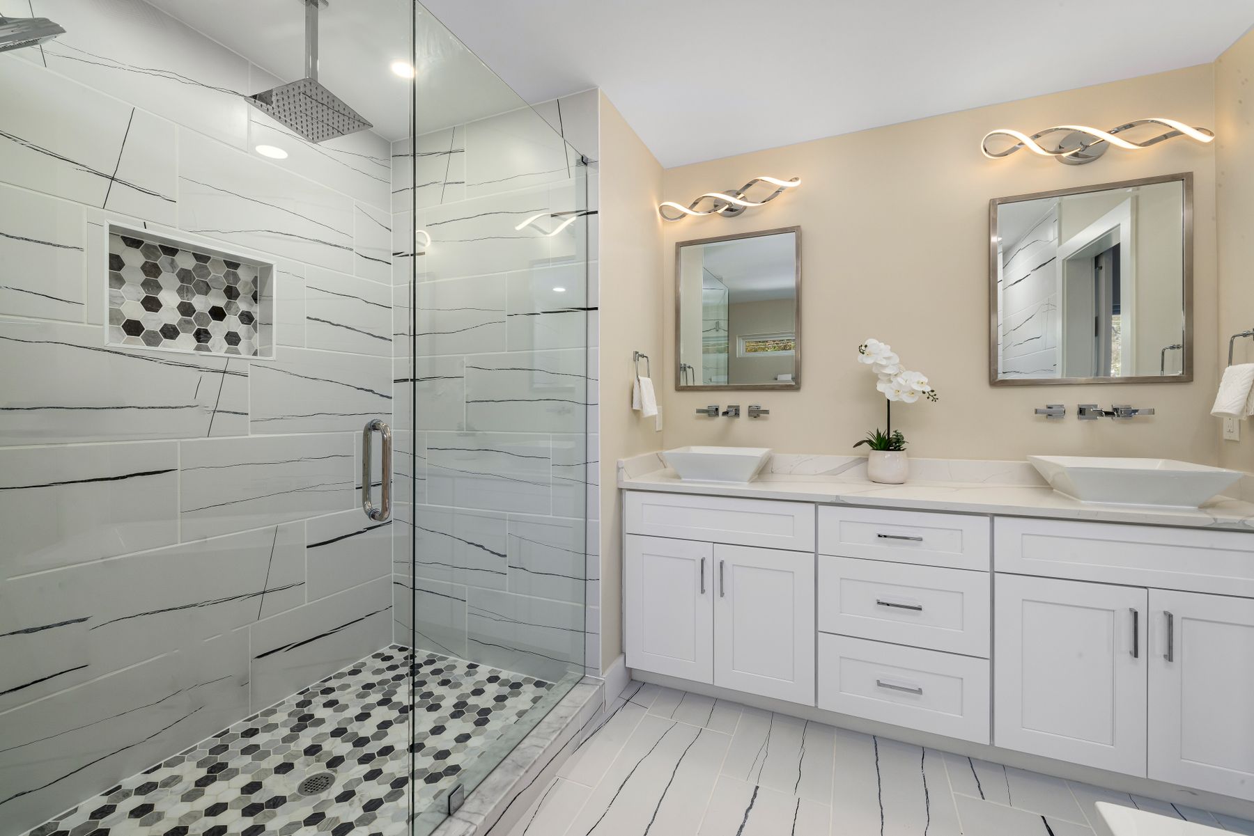 Bright bathroom with a glass shower, white double vanity and framed mirrors