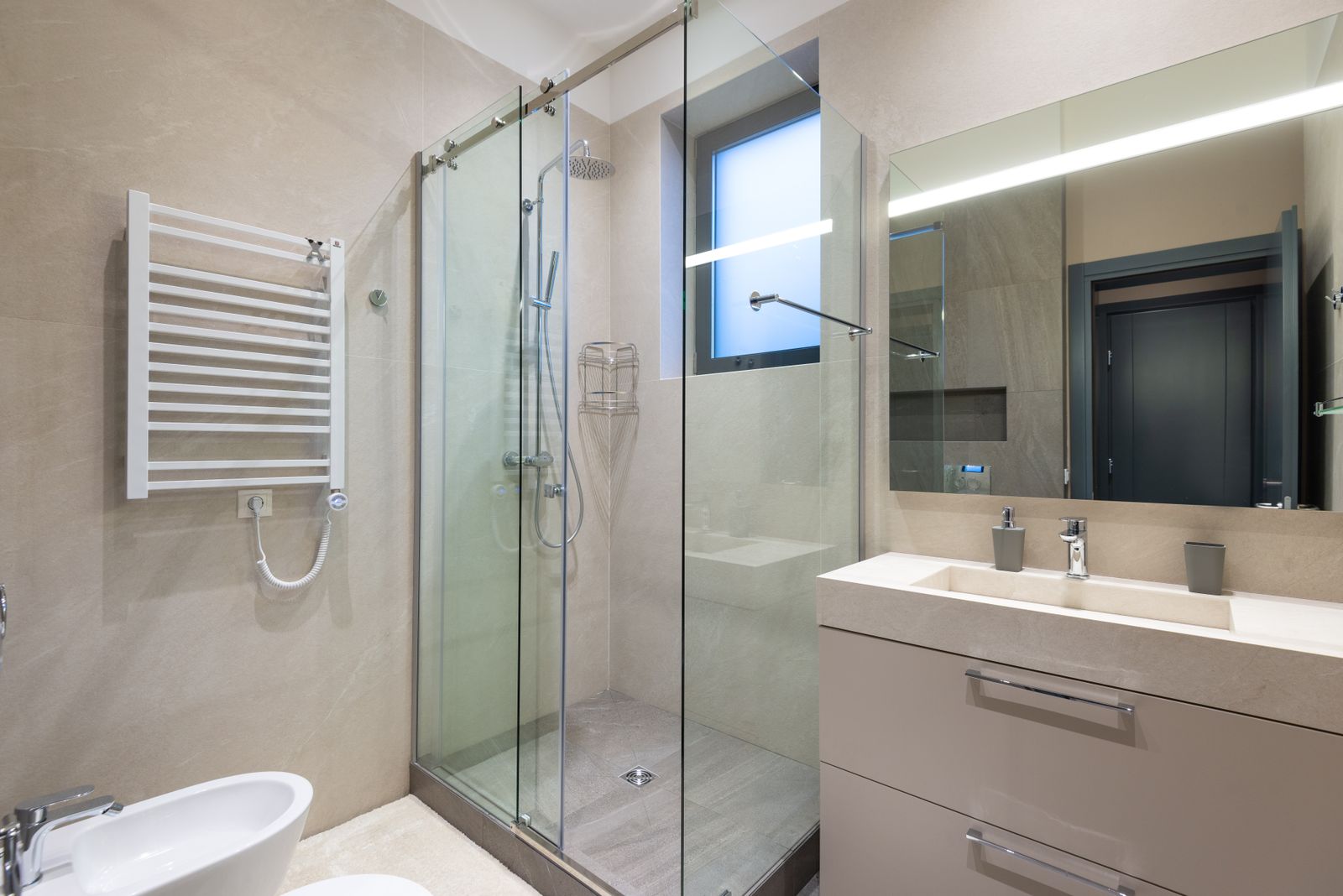 Glass shower enclosure with neutral wall finishes, a handheld shower and vanity